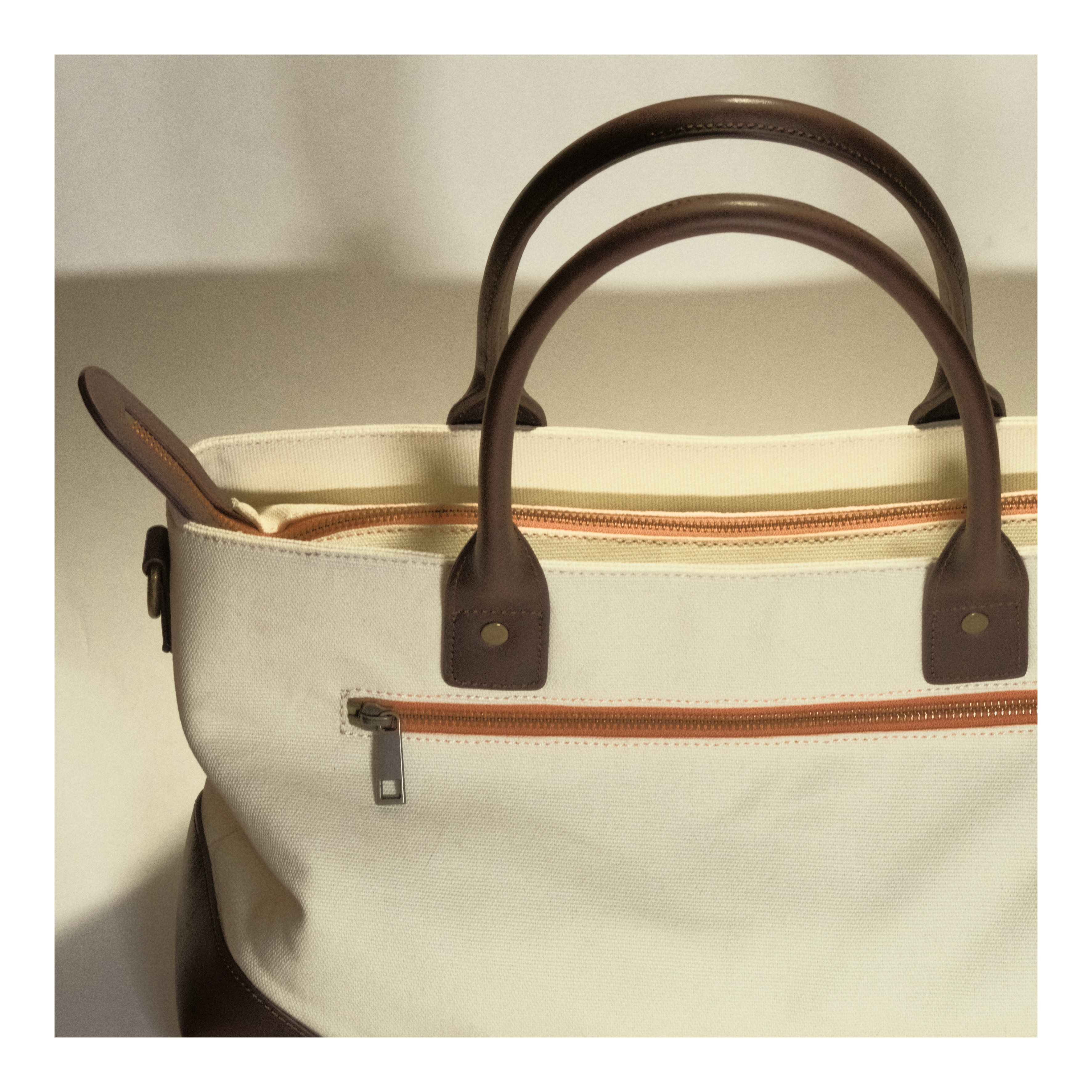 Beige canvas tote bag with brown leather handles and front zip pocket