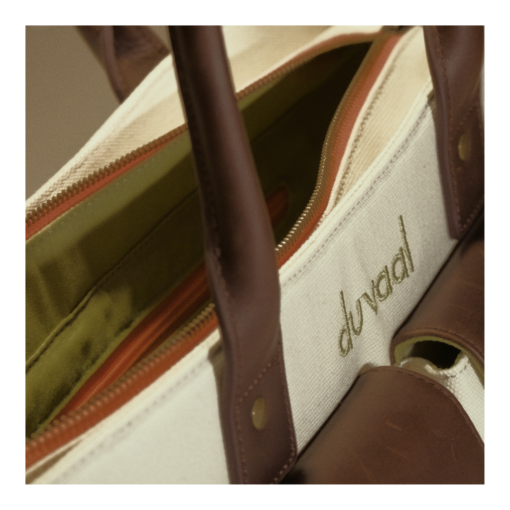 Close-up of canvas tote bag with brown leather handles and zippered compartment